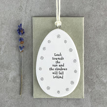 Load image into Gallery viewer, Porcelain Flat Hanging Ceramic Egg with message 'Look towards the sun and the shadows will fall behind.